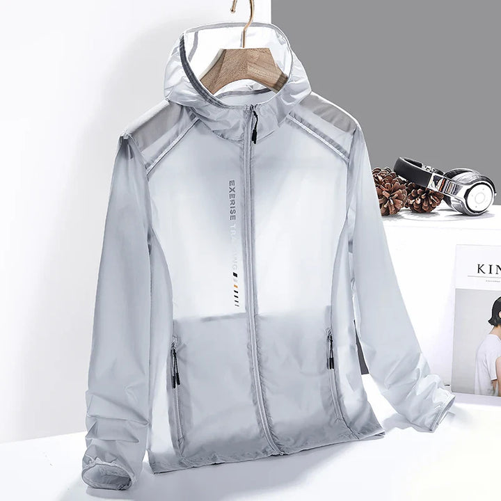 A light grey, semi-transparent hooded windbreaker jacket made of lightweight, quick-dry material is displayed on a wooden hanger. The jacket has black zipper pockets and EXERSE printed vertically on the front. Headphones and pinecones are in the background.