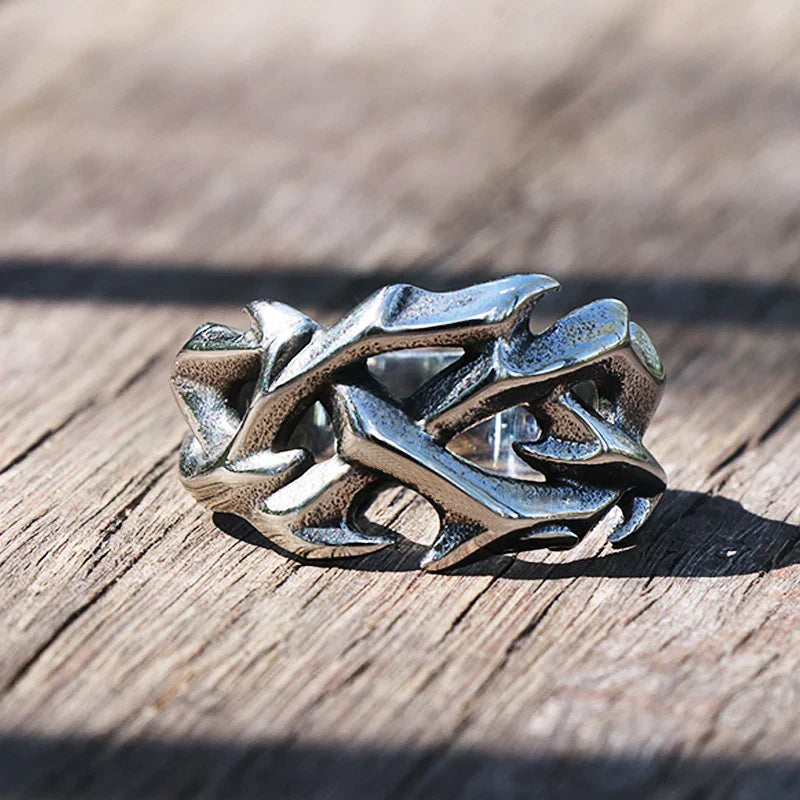 A striking fashion jewelry piece, this silver ring features an intricate, organic design resembling entwined branches or thorns, resting on a weathered wooden surface.