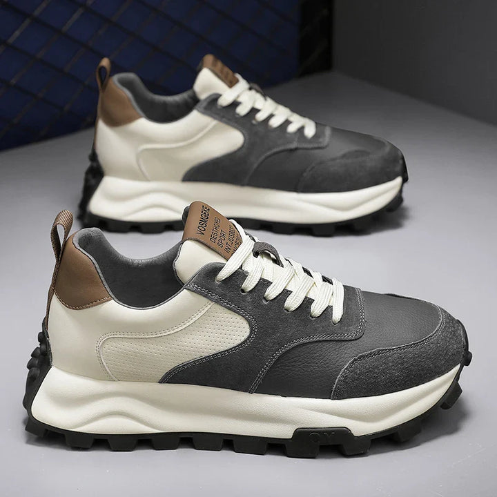 A pair of stylish multicolor sneakers with gray and white panels, brown accents on the heel and tongue, white laces, and chunky black outsoles, featuring cloud-like cushioning for all-day comfort, displayed on a gray surface.