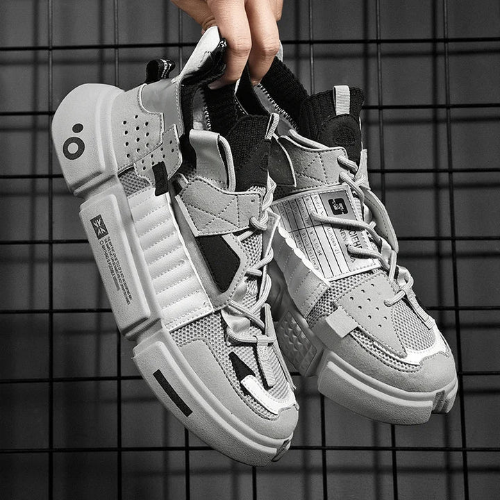 A hand holds up a pair of Extreme VS7 Sneakers—modern, chunky gray and white streetwear sneakers with mesh and leather details, black accents, bold stitching, and unique tags—set against a black metal grid background.