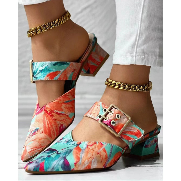 A pair of colorful floral-patterned, pointed-toe mules slippers with gold buckles and square heels, worn with white pants and chunky gold chain anklets—perfect summer shoes for a chic look.