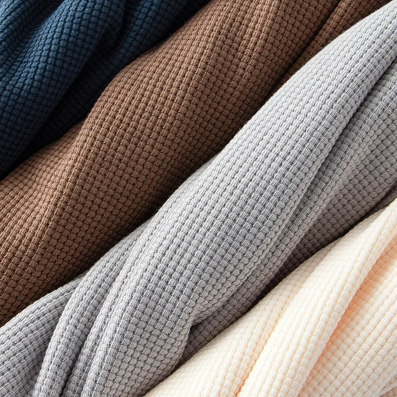 Four waffle knit fabrics are layered diagonally. The colors, from top to bottom, are dark blue, brown, light gray, and off-white. Each heavyweight shirt material is made from 260G cotton with visible texture and folds.