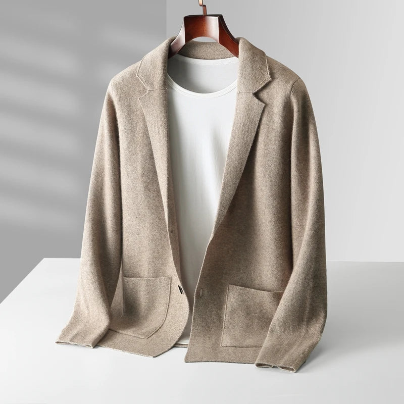 A beige men's wool cardigan blazer with front pockets is draped over a wooden hanger, layered atop a plain white T-shirt, and displayed on a white surface against a light gray background.