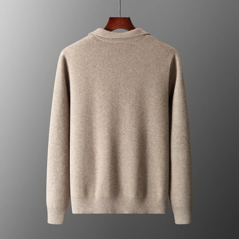 A beige, long-sleeve merino wool sweater is displayed on a wooden hanger against a plain gray background, shown from the back. The sweater has a simple design with ribbed cuffs and hem for natural temperature regulation.