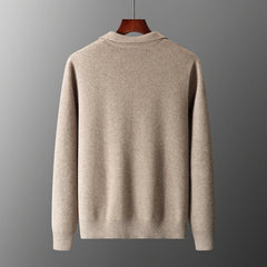 A beige, long-sleeve merino wool sweater is displayed on a wooden hanger against a plain gray background, shown from the back. The sweater has a simple design with ribbed cuffs and hem for natural temperature regulation.