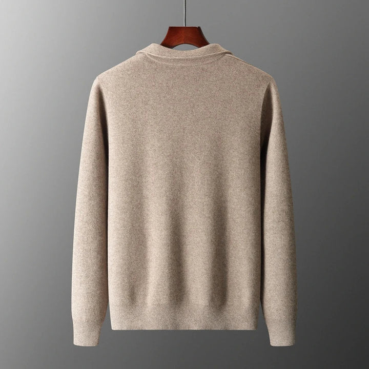 A beige, long-sleeve merino wool sweater is displayed on a wooden hanger against a plain gray background, shown from the back. The sweater has a simple design with ribbed cuffs and hem for natural temperature regulation.