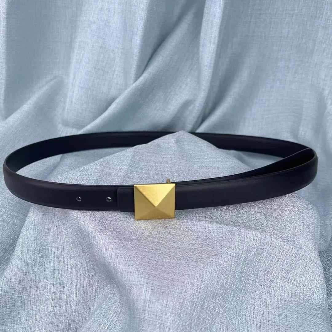 A black leather belt with an adjustable length and a large, square gold buckle displayed on a light gray textured fabric background.