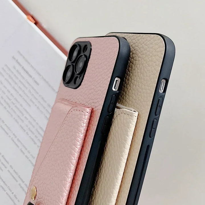 Two smartphones with pebble-texture leather cases, one pink and one beige, are shown side by side. Each features a cardholder pocket with a gold button detail, set against the backdrop of a blurred open book.