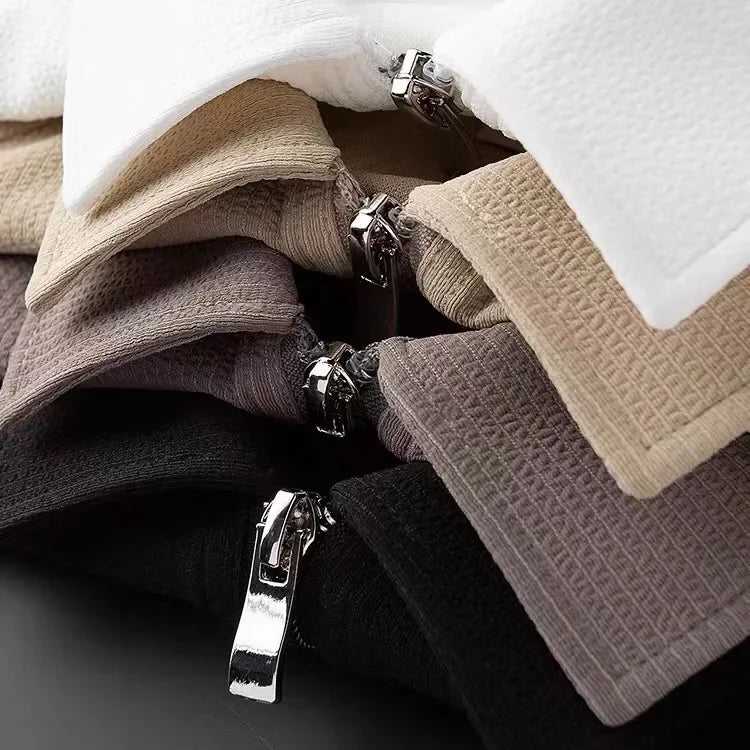 A close-up of six folded garments in neutral shades—white, beige, taupe, gray, and black—each featuring a visible metallic zipper pull and textured moisture-wicking fabric perfect for a mens silk polo shirt.