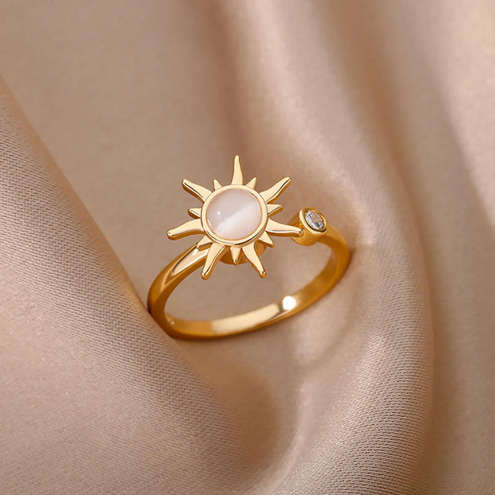 A sun ring with a central white stone and a small clear gem on the band, displayed on soft beige fabric. This adjustable gold ring captures celestial elegance in every detail.