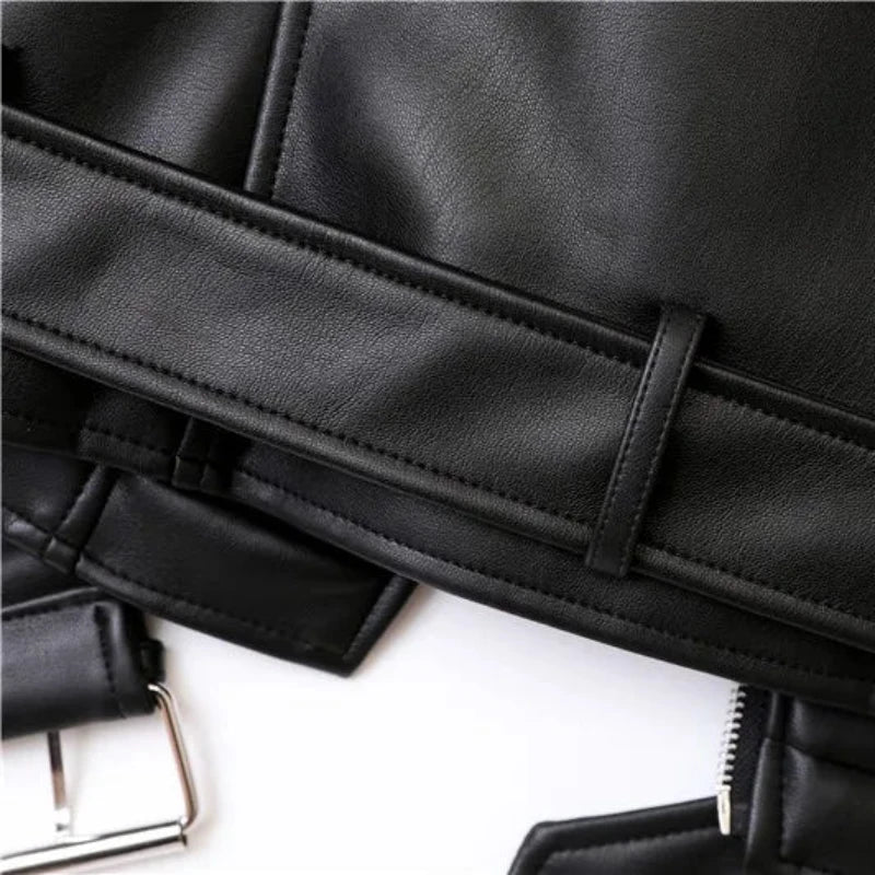 Close-up of a black faux leather jacket, showing detailed stitching, a belt loop, part of an adjustable waist belt buckle, and a zipper. The texture of the material and seam lines are visible.