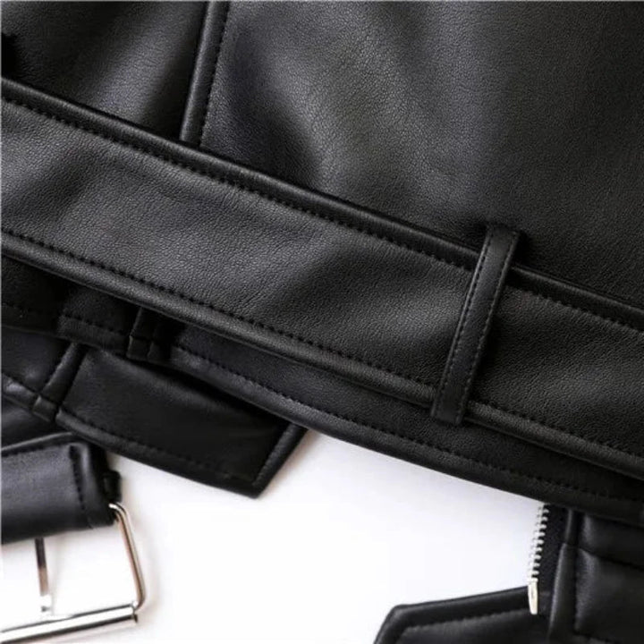 Close-up of a black faux leather jacket, showing detailed stitching, a belt loop, part of an adjustable waist belt buckle, and a zipper. The texture of the material and seam lines are visible.