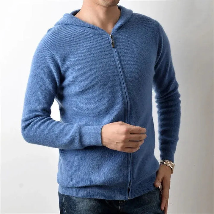 A man wearing a luxurious cashmere zip-up hoodie and jeans stands against a plain white background, with one hand adjusting his sleeve and the other resting on his waist. His face is partially out of frame.