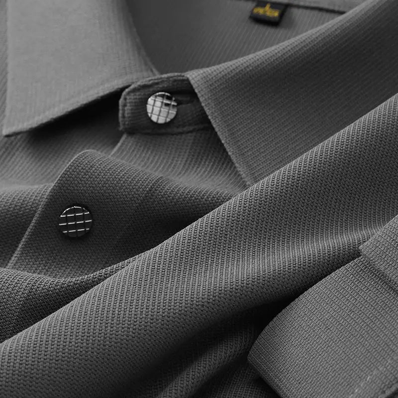 Close-up of a wrinkle-resistant button-up dress shirt in textured gray, highlighting the fabric weave and two black buttons with a white grid pattern. The collar and part of the shirt are neatly folded.