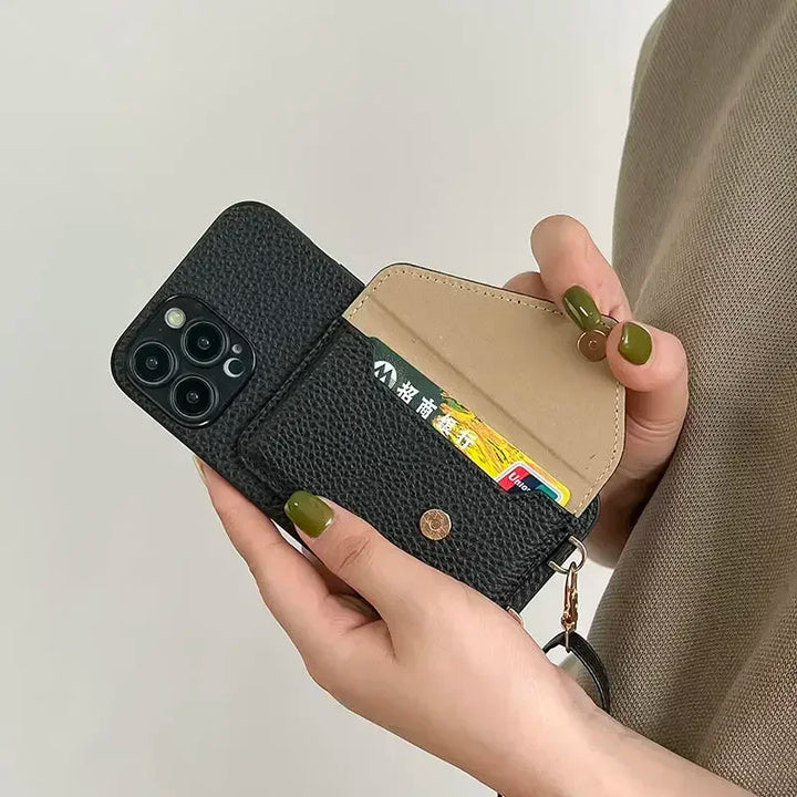 A person holds a black pebble-texture phone case with a wallet compartment open, showing cards inside the cardholder pocket. Their nails are painted olive green, and they wear a beige top.