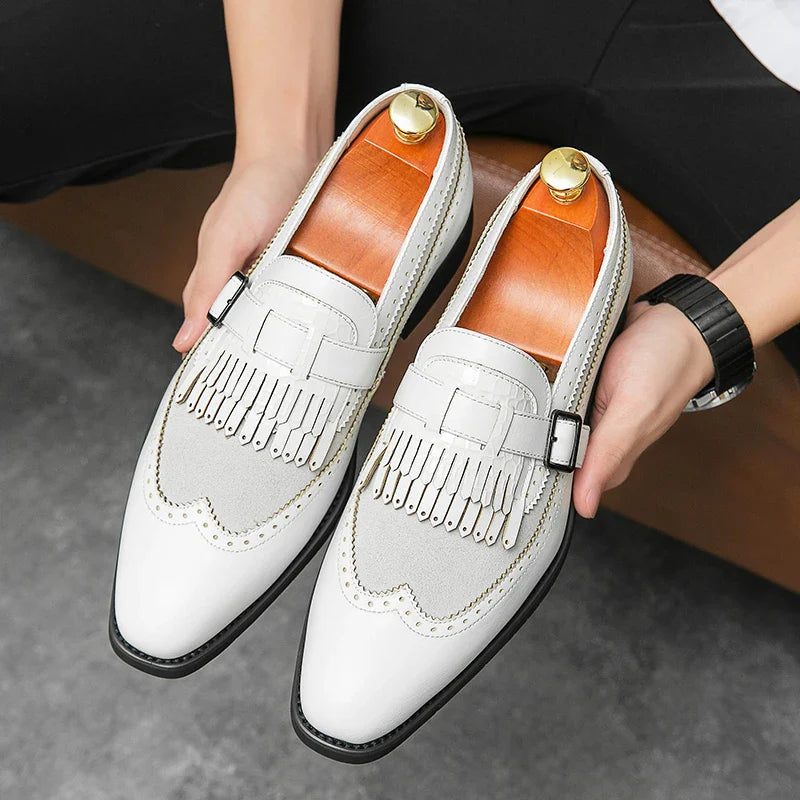 A person holds a pair of stylish white and light gray premium leather shoes with fringe detailing and metallic accents, featuring orange-brown insoles, black soles, and a convenient slip-on design.