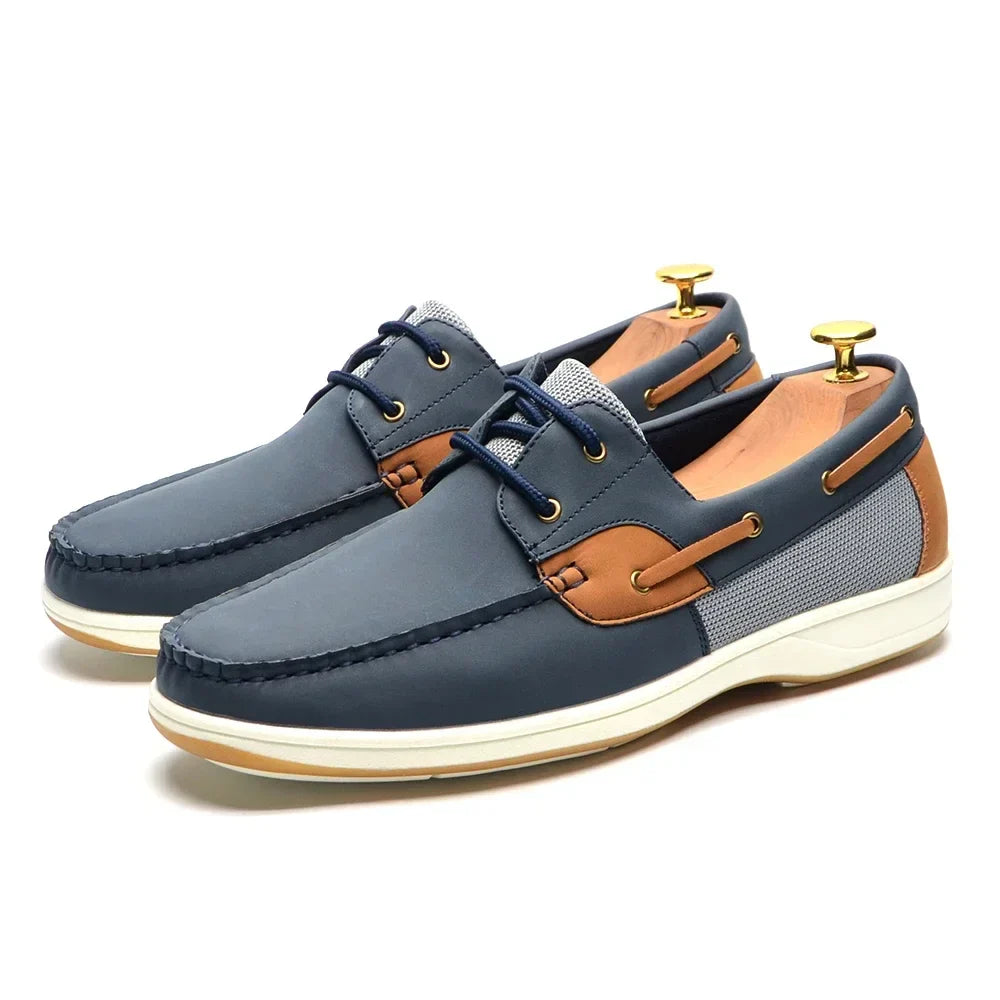 A pair of fashionable men's shoes, these blue and brown boat shoes with white soles feature navy laces, tan accents, and a mesh side panel, displayed with shoe trees inserted.