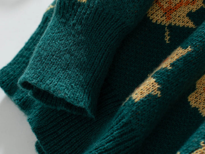 Close-up of a soft knit material green sweater sleeve with a ribbed cuff and part of a tan and yellow maple leaf pattern visible. The texture of the comfortable sweater is clearly shown.