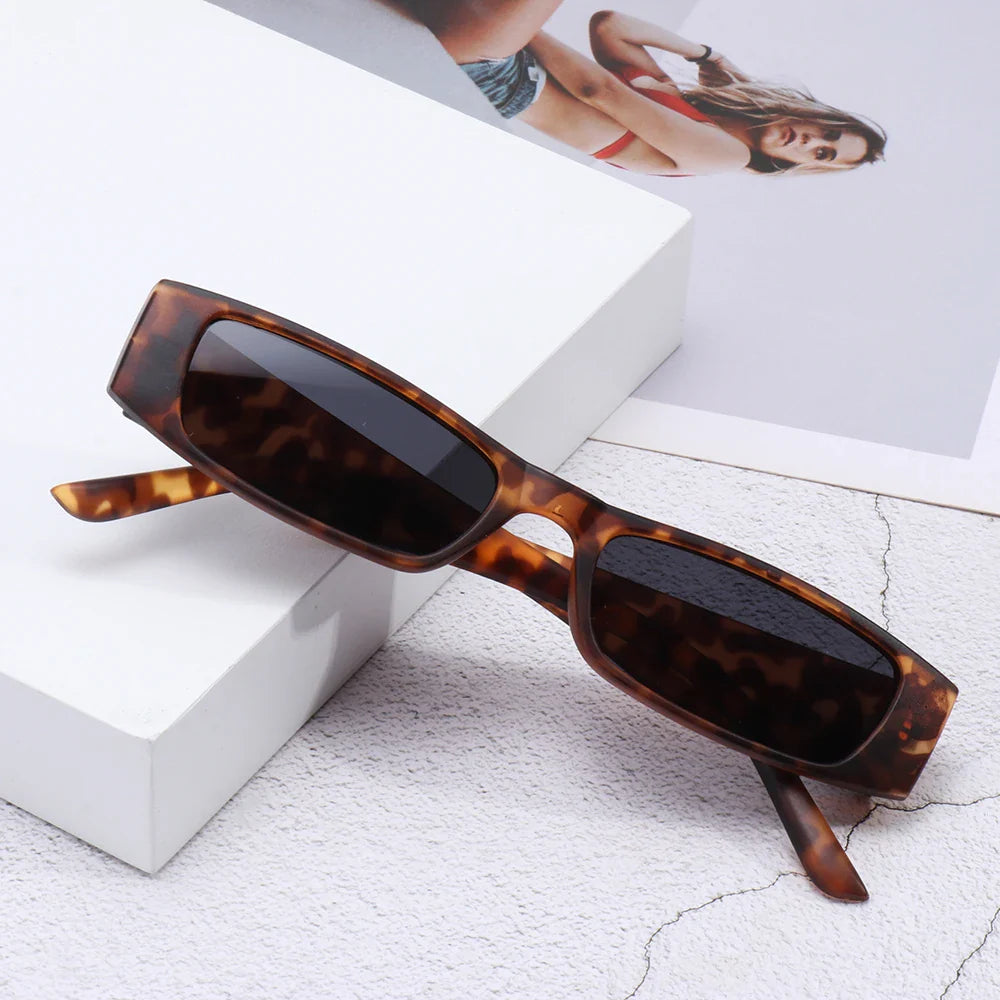 Retro rectangle sunglasses with a lightweight frame and dark lenses rest on a white surface, next to a photo of a woman in a swimsuit.