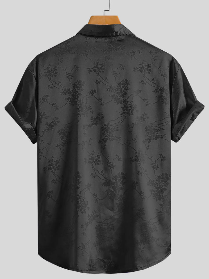 A short-sleeved, button-up black shirt with a subtle floral pattern made from breathable fabric, displayed on a wooden hanger against a plain light gray background.