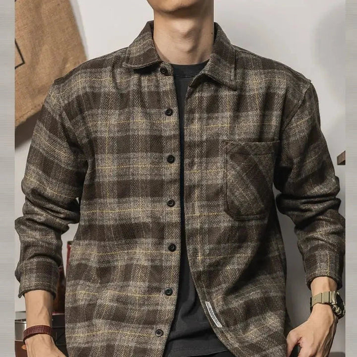 A person wearing a relaxed fit brown and gray plaid button-up shirt with long sleeves, a chest pocket, and black undershirt—perfect for layering. The persons face is not visible.