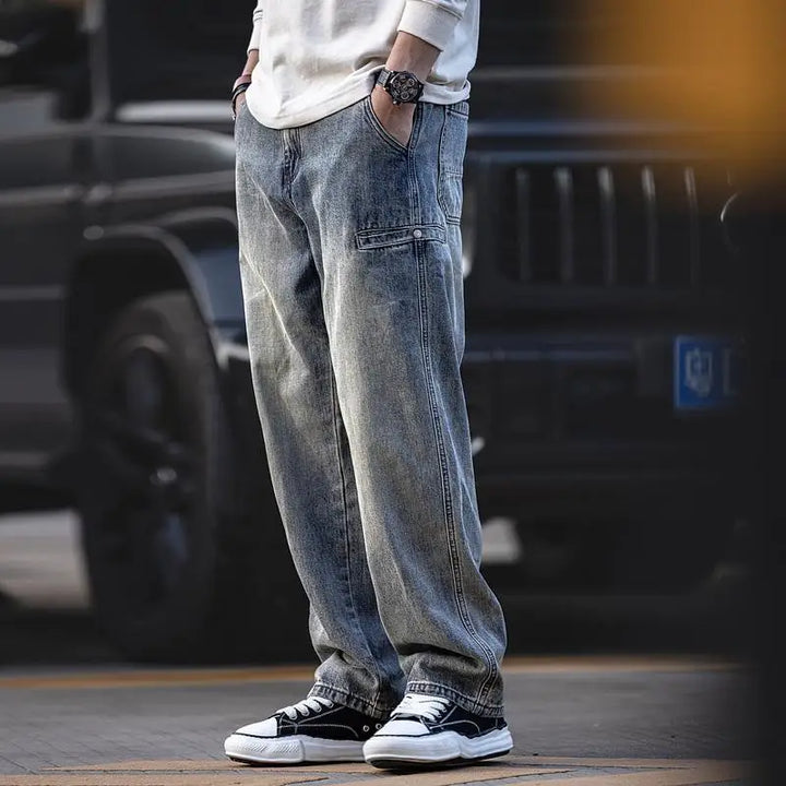 A person wearing classic fit blue straight leg jeans, a white long-sleeve shirt, black-and-white sneakers, and a watch stands outdoors with hands in pockets; a dark vehicle is blurred in the background.