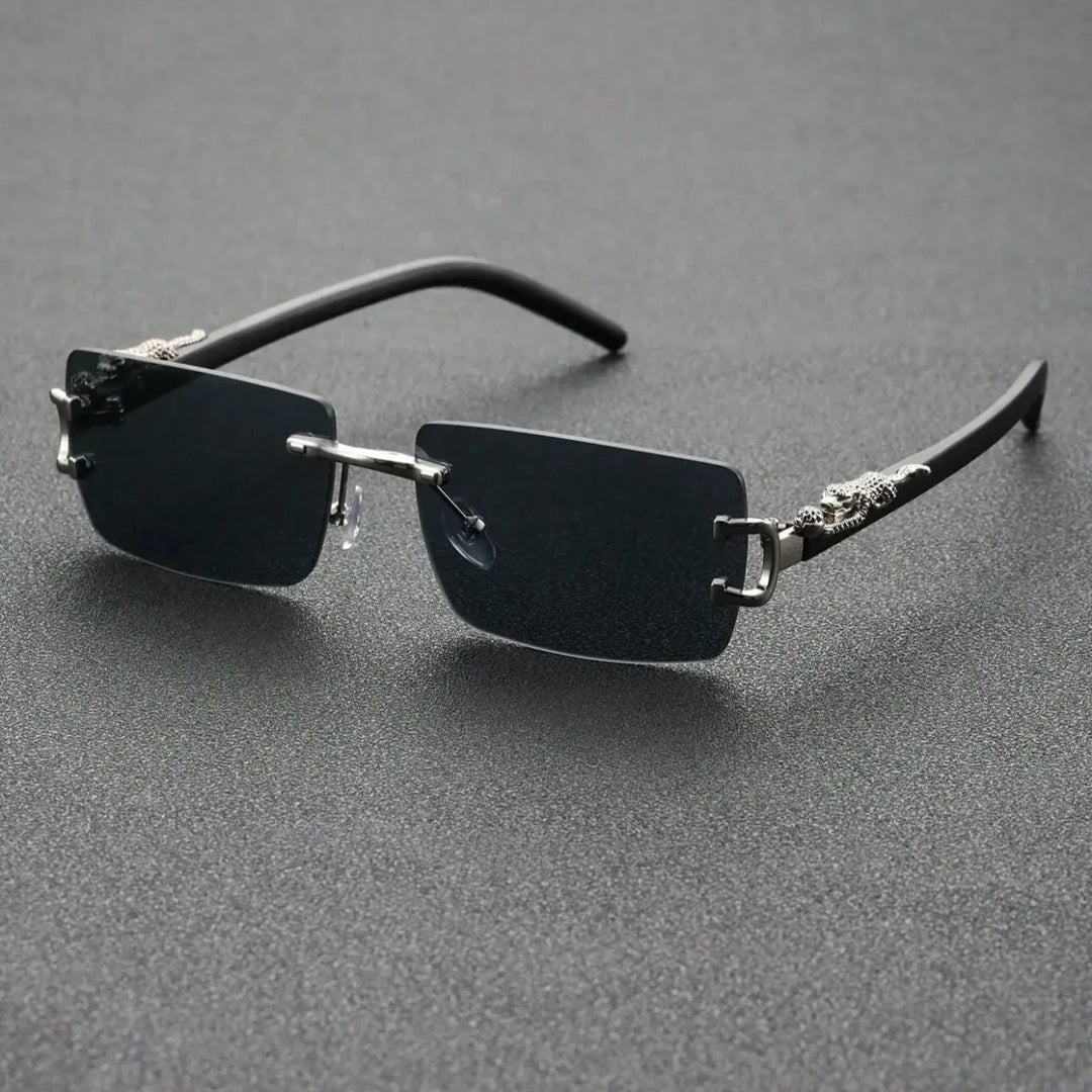 Rectangular, rimless black sunglasses with thin metal bridge and temples, featuring durable hinges and decorative silver accents near the hinges, displayed on a textured dark surface.