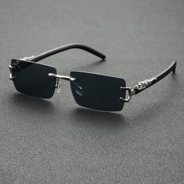Rectangular, rimless black sunglasses with thin metal bridge and temples, featuring durable hinges and decorative silver accents near the hinges, displayed on a textured dark surface.