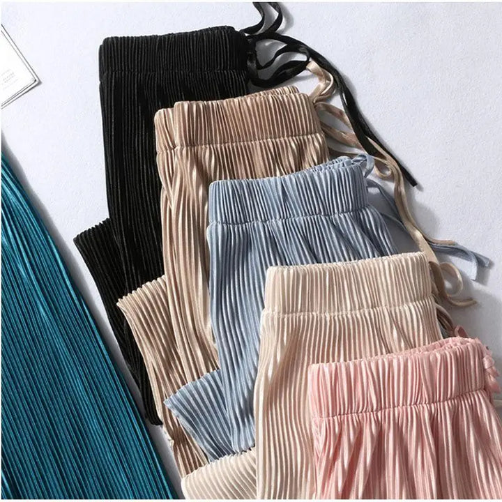 Five pairs of Pleated Ice Silk wide leg pants in black, beige, blue, light beige, and pink are neatly layered on a flat surface, with an additional teal pleated garment partially visible on the left side.