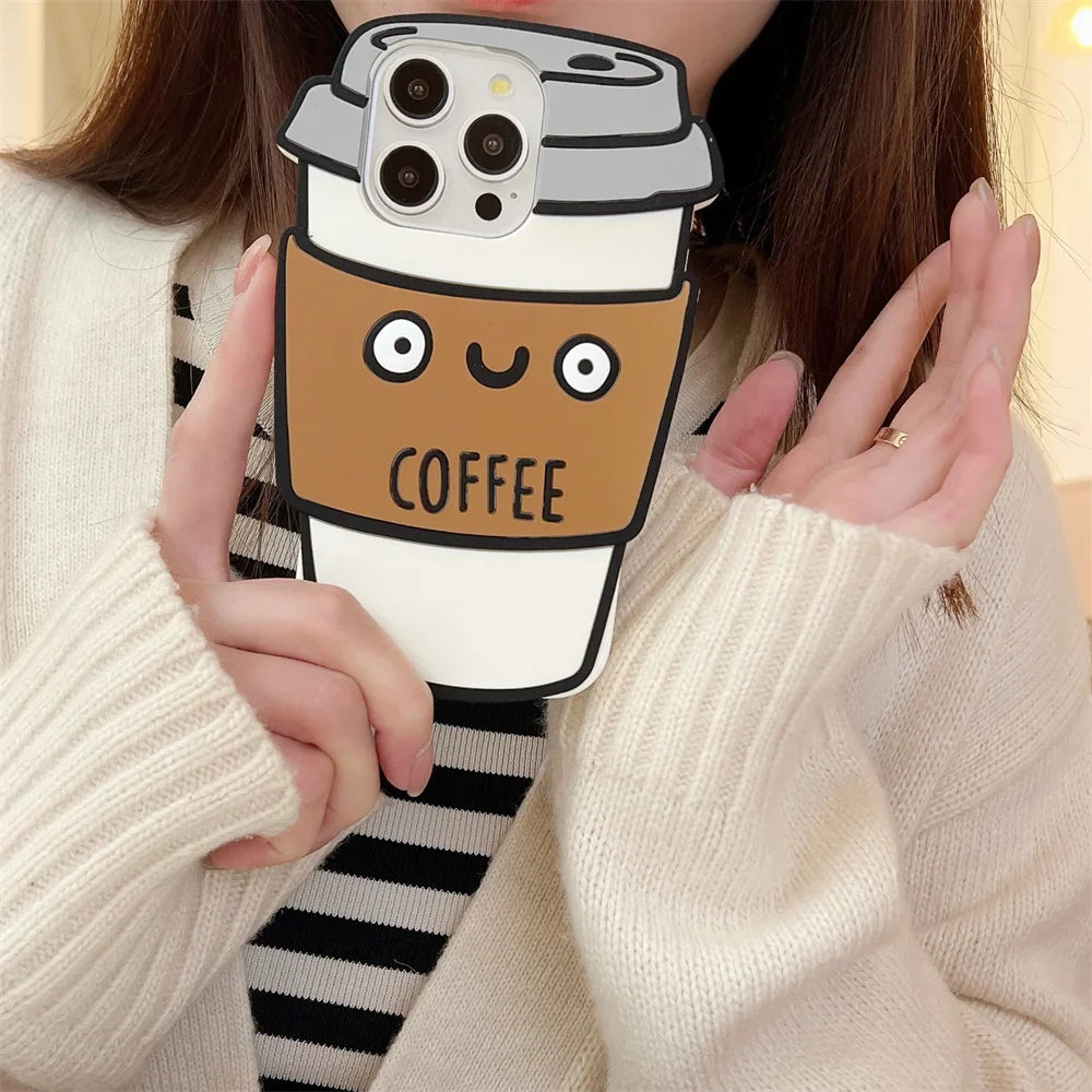 A person holds a phone with a 3D coffee cup case labeled COFFEE, made of soft silicone for shockproof protection. They wear a cream sweater over a black-and-white striped top, partially covering their face with the phone.