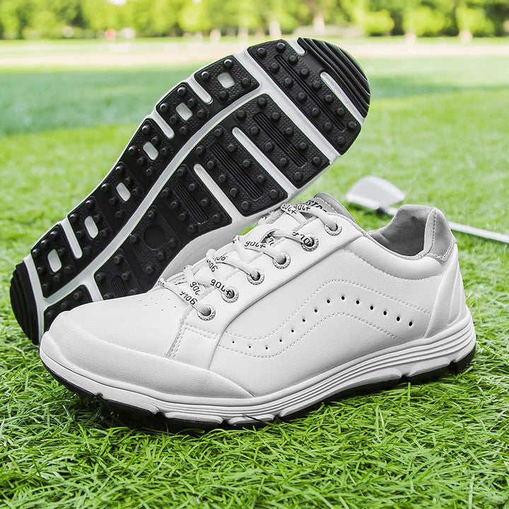 A pair of white waterproof golf shoes with black soles displayed on green grass, one lying on its side to show the advanced cleat technology tread pattern and the other upright; a golf club is visible in the background.