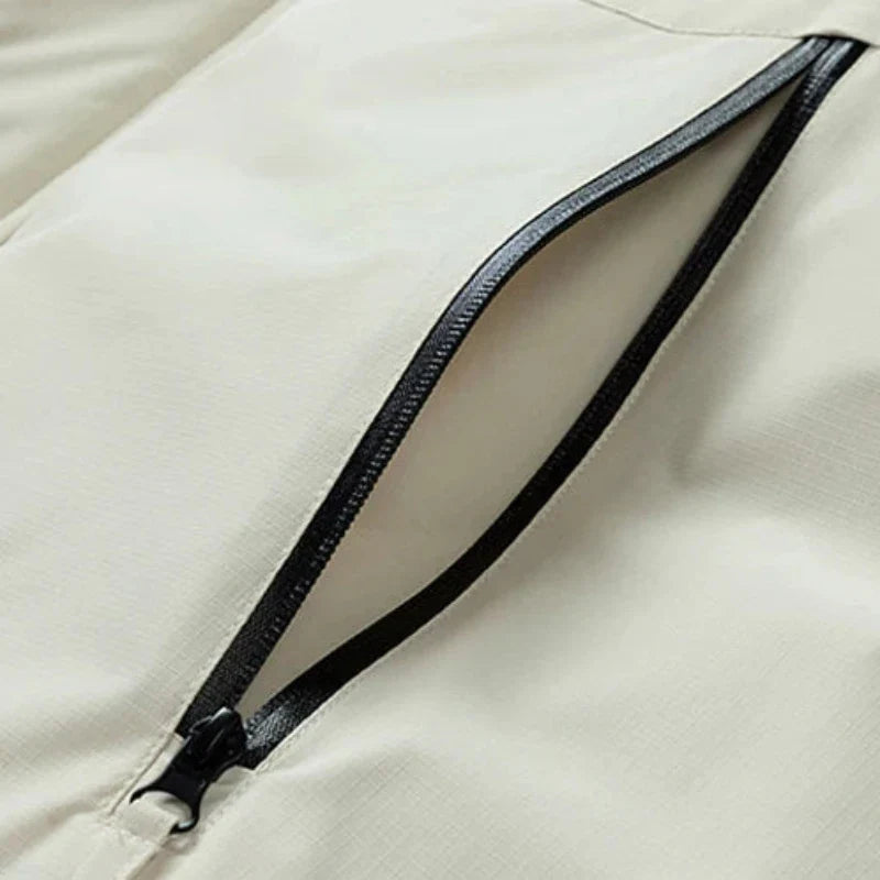 Close-up of a partially open black zipper on a light beige, windproof fabric, likely part of a jacket or bag. The zipper reveals the clean stitching and smooth texture of the material.