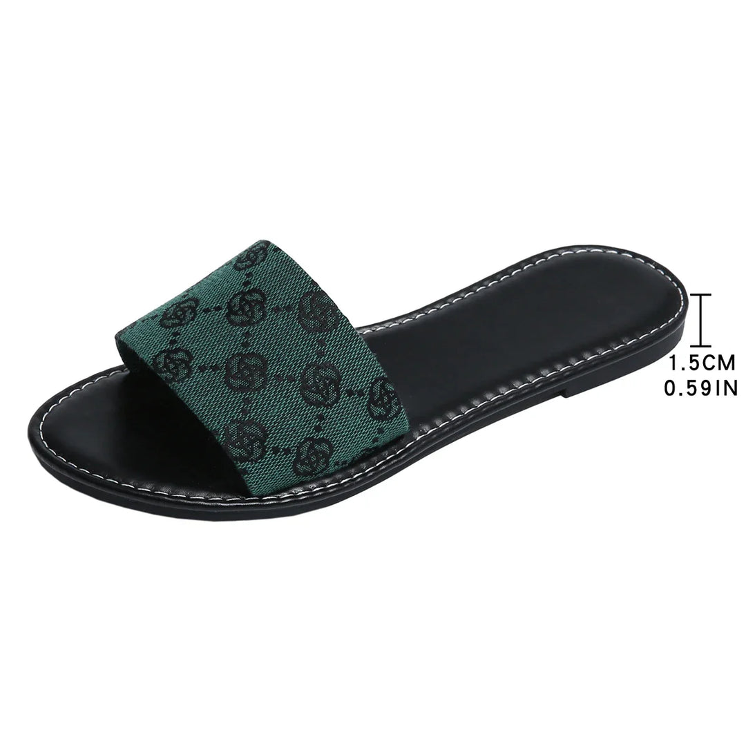 A black slide sandal with a green fabric strap featuring a black pattern, this slide silhouette from French Sole boasts white stitching along the sole edge and a comfortable 1.5 cm (0.59 inch) heel—timeless shoes for any wardrobe.