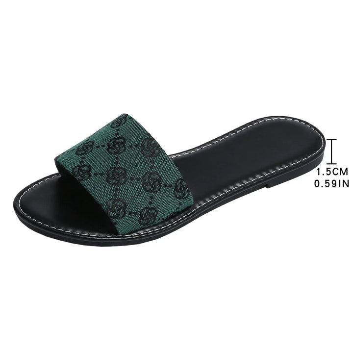 A black slide sandal with a green fabric strap featuring a black pattern, this slide silhouette from French Sole boasts white stitching along the sole edge and a comfortable 1.5 cm (0.59 inch) heel—timeless shoes for any wardrobe.