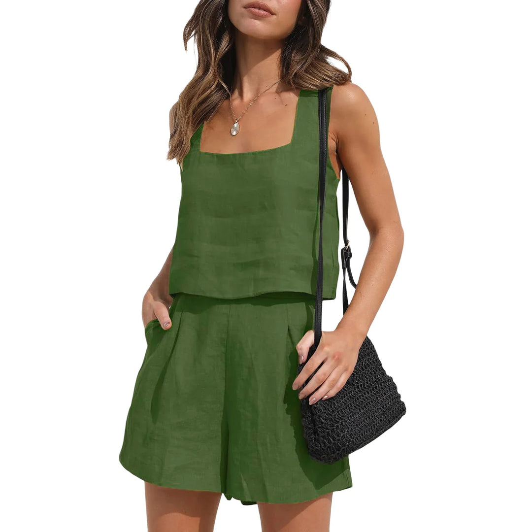 A woman in a sleeveless green linen set stands with one hand in her pocket, holding a black woven shoulder bag. Her wavy brown hair and necklace add to the contemporary style against a clean white background.
