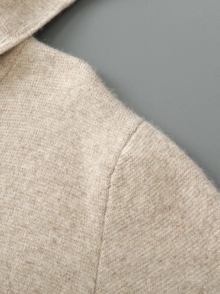 Close-up of the shoulder and hood of a beige autumn winter sweater, highlighting the soft texture and detailed stitching on a gray background.