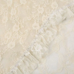 Close-up of cream-colored silky lace fabric with delicate patterns and a gathered ruffled edge running diagonally across the image, evoking an asymmetrical hemline.