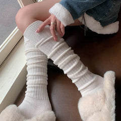 A person wearing cozy, breathable socks and fluffy slippers sits by a window on a brown seat, dressed in a denim jacket with white fur trim, gently touching one sock made from a soft Cashmere cotton blend.