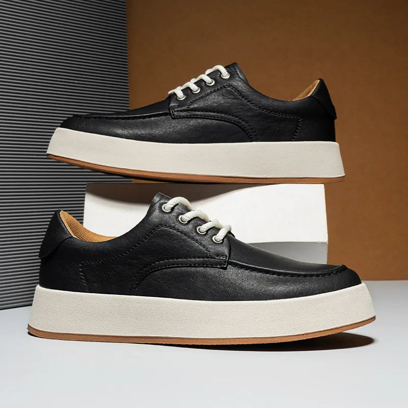 A pair of black leather sneakers, inspired by Italian designer shoes, with white laces and thick white soles are displayed stylishly—one balanced on a white box, the other resting on a flat surface.
