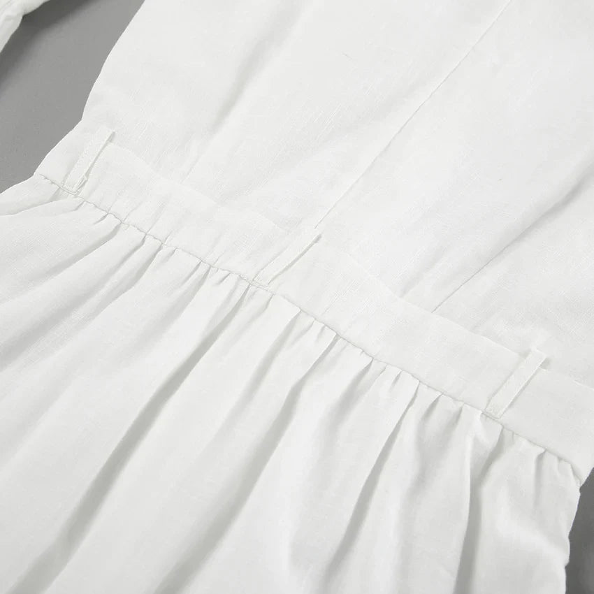 Close-up of a chic romper in white linen, featuring a gathered waist with visible seams and pleats—perfect for a summer outing, displayed on a flat surface.