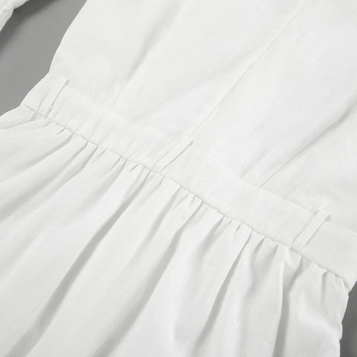 Close-up of a chic romper in white linen, featuring a gathered waist with visible seams and pleats—perfect for a summer outing, displayed on a flat surface.