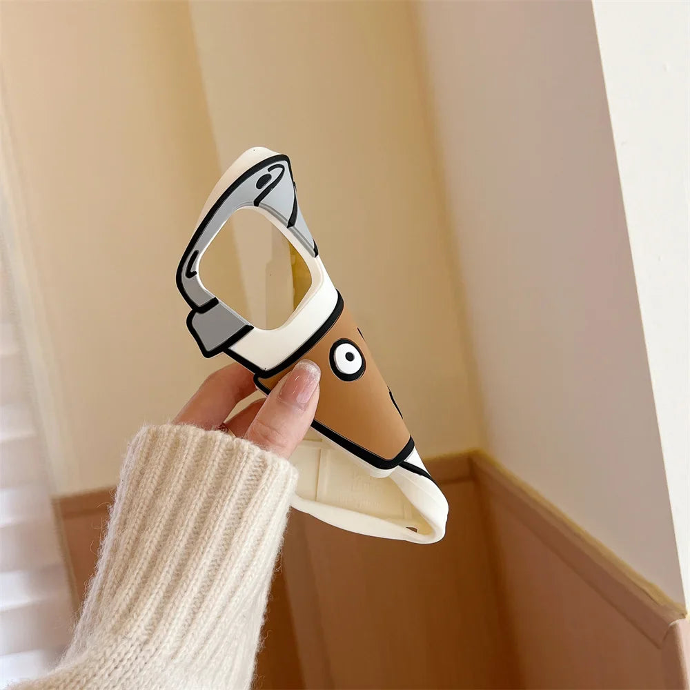 A hand in a beige sweater holds a soft silicone phone case shaped like a cartoon dog with a raised ear, tan face, and big white eyes, offering shockproof protection in a softly lit room with light brown and white walls.