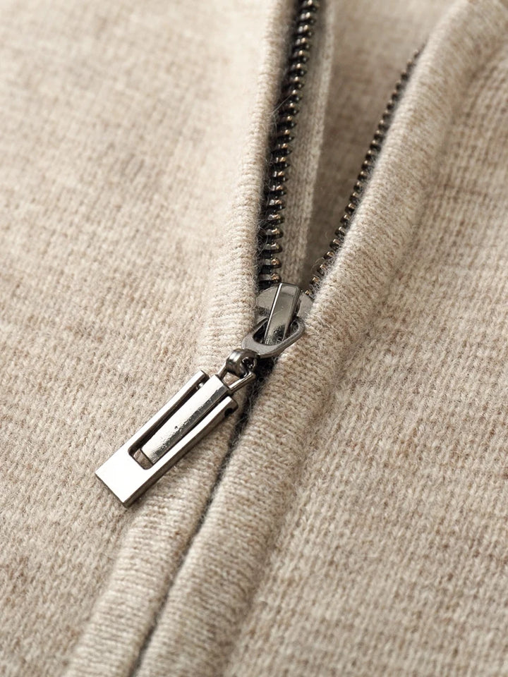 Close-up of a silver metal zipper partially unzipped on a soft, light beige knit wool cardigan, highlighting the texture of the material and the detailed zipper pull and teeth.