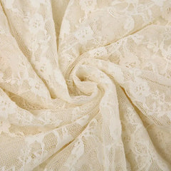Close-up of silky lace fabric with a floral pattern, arranged in a swirling, circular fold. The delicate texture and intricate design are clearly visible.