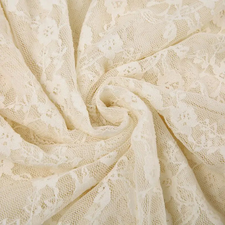 Close-up of silky lace fabric with a floral pattern, arranged in a swirling, circular fold. The delicate texture and intricate design are clearly visible.