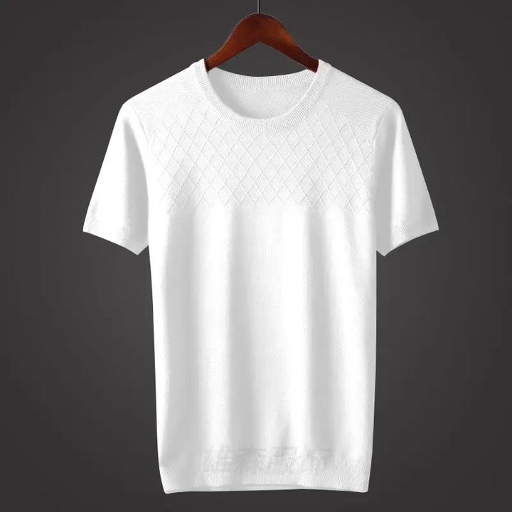 A classic fit white short-sleeve knit sweater hangs on a wooden hanger against a dark background. The upper chest area features a subtle diamond-pattern, while the rest of the sweater is smooth.