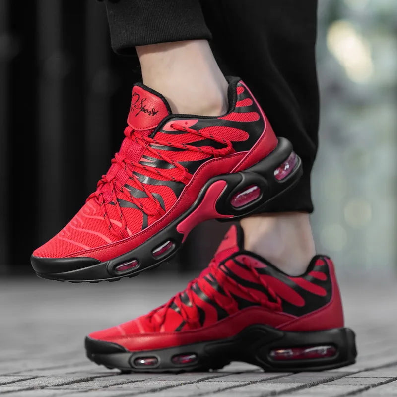 A person wearing bright red and black athletic sneakers with a breathable mesh upper and visible air-cushion soles stands on a wooden surface; only the lower legs and shoes are visible.