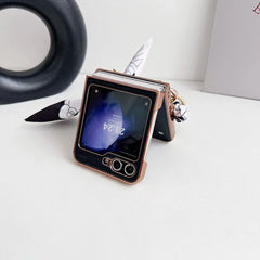 A Samsung Galaxy Z Flip in a premium leather case is partially open and standing on a white surface. A patterned ribbon is attached for style, while the screen displays the time as 21:24, offering both elegance and shockproof protection.
