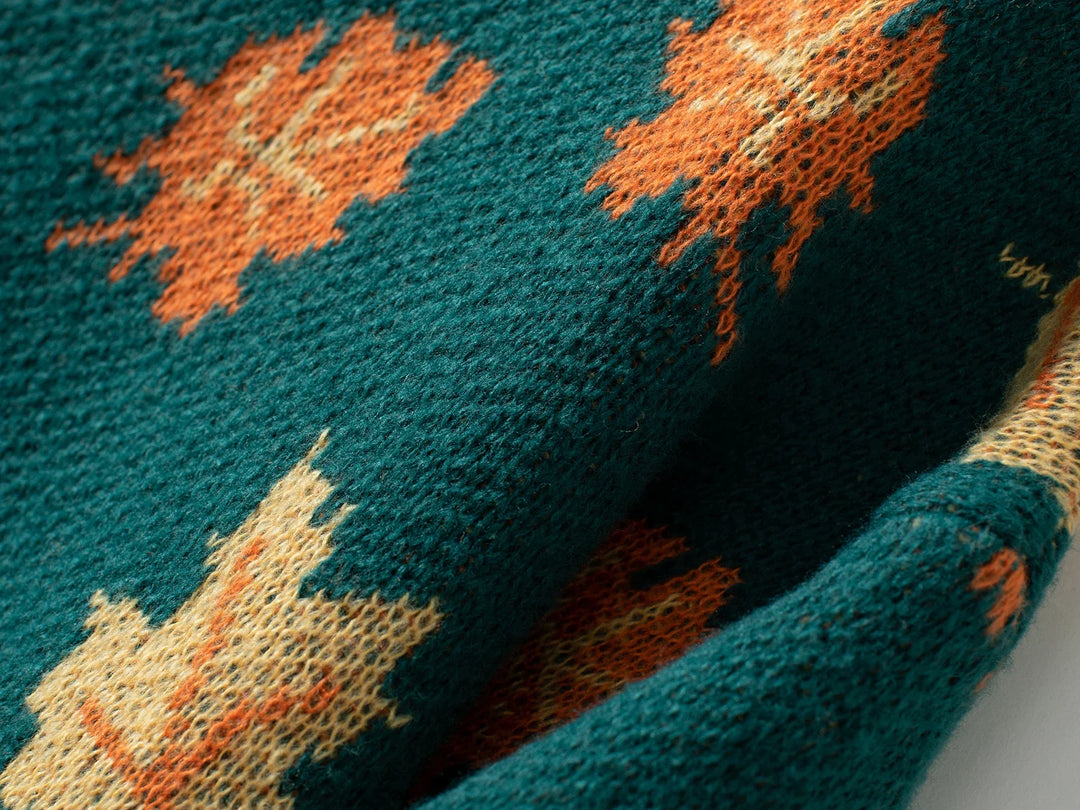 Close-up of a comfortable sweater in textured green fabric featuring an orange maple leaf pattern. The soft knit material appears slightly fuzzy, with visible weave details and overlapping sections.