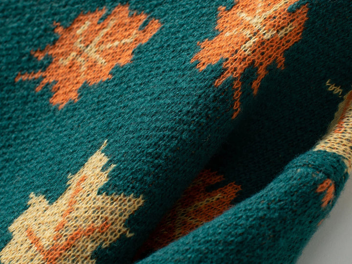Close-up of a comfortable sweater in textured green fabric featuring an orange maple leaf pattern. The soft knit material appears slightly fuzzy, with visible weave details and overlapping sections.